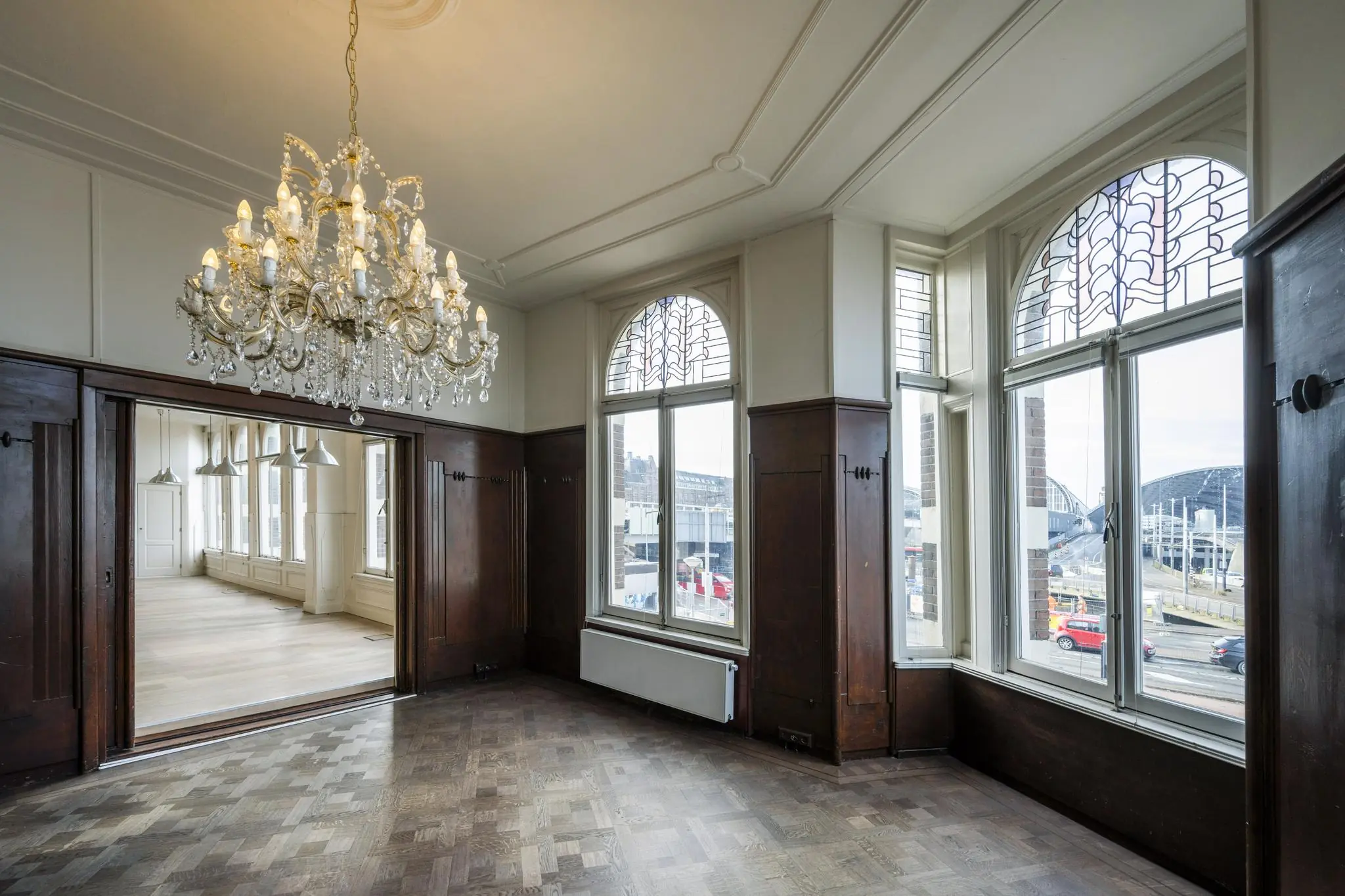 Stijlvol interieur aan de De Ruijterkade met houten lambrisering, kristallen kroonluchter en uitzicht op Amsterdam Centraal Station.